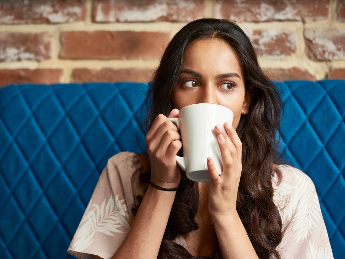 A woman sitting on a couch drinking a cup of coffee.