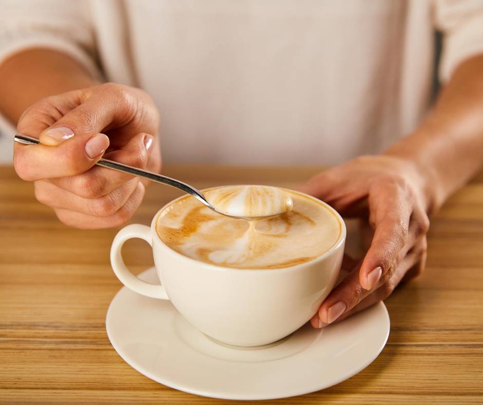 A woman's hand holding a spoon in a cup of coffee.