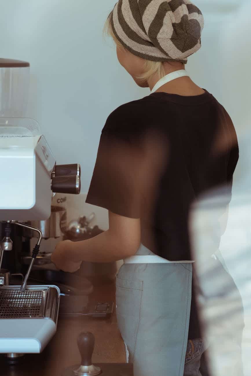crop slim female barista in knit hat preparing fresh coffee