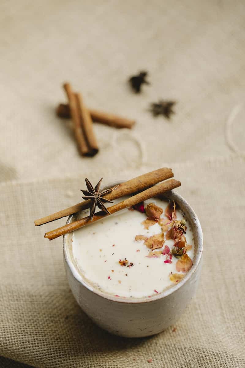From above composition of tasty homemade chai tea served in ceramic mug with star anise on sticks of cinnamon and other spices placed on gray linen tablecloth