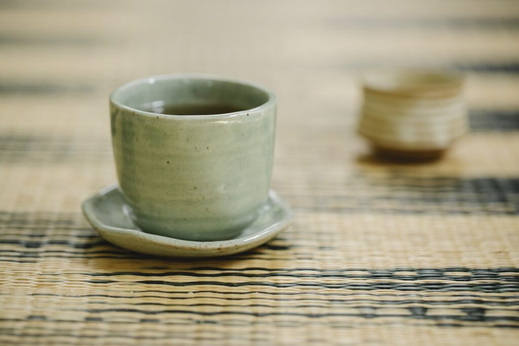 Round shaped oriental cups of hot fresh tea with saucer on ornamental mat in daytime